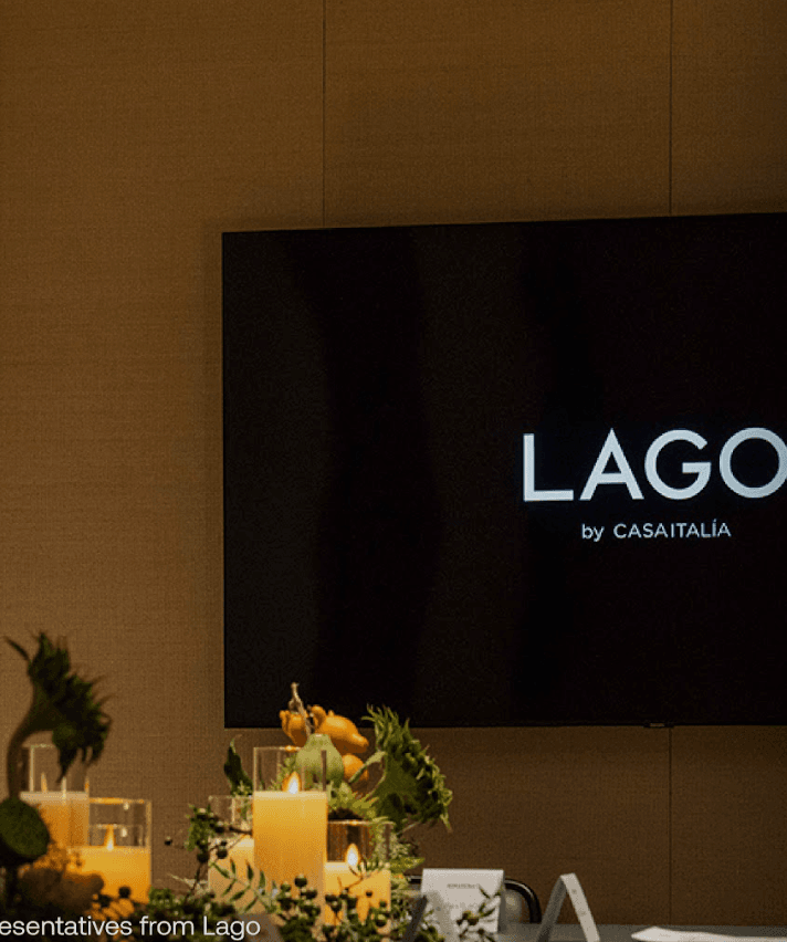 Screen displaying LAGO by CASAITALIA at an event with candles and foliage on a table