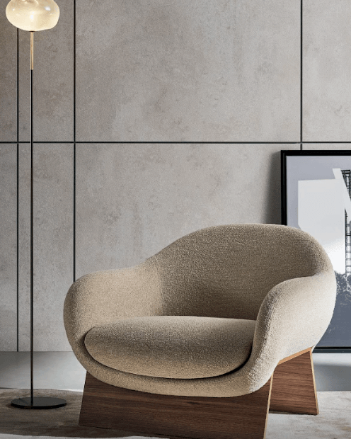 Elegant beige curved armchair with wooden base against concrete wall